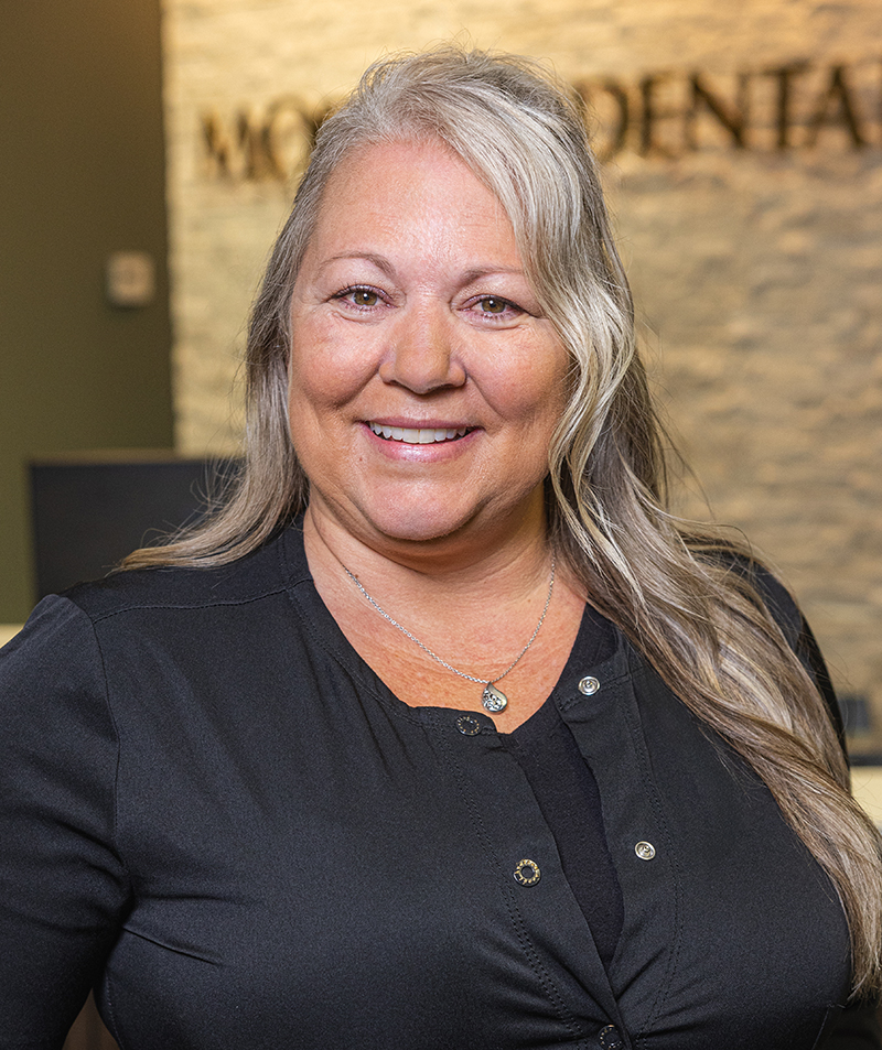 Woman with long gray hair smiling at Modern Dental office reception area